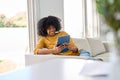 Smiling young African woman using digital tablet relaxing on couch at home. Royalty Free Stock Photo