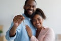 Smiling young afro american couple hugging and show keys to new property at home interior Royalty Free Stock Photo