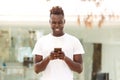 Smiling young afro american man using mobile phone standing outdoors in city Royalty Free Stock Photo