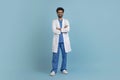 Smiling young arab doctor man posing with folded arms over blue background Royalty Free Stock Photo