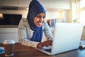 Smiling young Arabic woman using a laptop in her kitchen