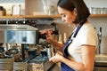 Smiling young asian barista girl, using coffee machine steamer, steaming milk for cappuccino order, standing in apron Royalty Free Stock Photo