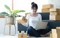 Smiling young Asian business owner woman prepare parcel box and standing check online orders of product for deliver to customer on Royalty Free Stock Photo