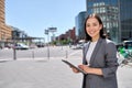 Smiling young Asian business woman standing on city street using digital tablet. Royalty Free Stock Photo