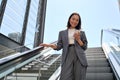 Smiling young Asian business woman standing on escalator using phone. Royalty Free Stock Photo