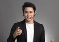 Smiling young asian businessman talking on headset against gray background Royalty Free Stock Photo