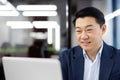 Smiling young Asian businessman working on laptop in office, sitting at table and working online, video calling Royalty Free Stock Photo