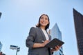 Smiling young Asian businesswoman using digital tablet on city street.