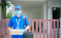 A smiling young asian delivery in blue uniform with parcel cardboard in front of customer house