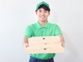 Smiling young Asian delivery man in green T-shirt uniform and cap holding pizza boxes on white background, giving box on camera, Royalty Free Stock Photo