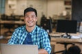 Smiling young Asian designer using a laptop at his desk Royalty Free Stock Photo