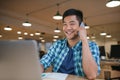 Smiling Asian designer talking on a cellphone in an office Royalty Free Stock Photo