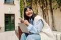 Smiling asian girl using mobile phone and laptop while sitting outdoors Royalty Free Stock Photo