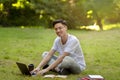 Smiling young asian guy sitting on grass with computer, studying outdoors Royalty Free Stock Photo