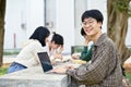 Smiling young Asian male college student with his laptop sits at a table in a campus park Royalty Free Stock Photo