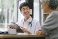 Smiling young asian male doctor with tablet pc computer talking to senior woman patient at hospital. Royalty Free Stock Photo