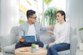 Smiling young Asian male psychiatrist talking to young woman at his office