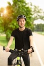 Smiling young asian man dressed in casual clothes and helmet riding a bicycle along the bike path in a city park Royalty Free Stock Photo