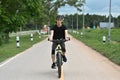 Smiling young asian man dressed in casual clothes and helmet riding a bicycle along the bike path in a city park Royalty Free Stock Photo