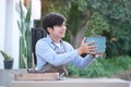 Smiling young asian man holding potted plant while sitting at backyard. Hobbies, leisure, home gardening concept Royalty Free Stock Photo