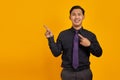 Smiling young Asian man pointing fingers at copy space on yellow background