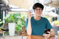 A smiling young Asian man showing his credit card while sitting at a wooden table outdoors Royalty Free Stock Photo