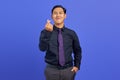 Smiling young Asian man showing love gesture sign on purple background