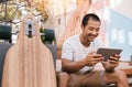 Smiling young Asian man sitting outside using a tablet Royalty Free Stock Photo