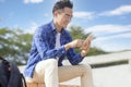 Smiling young asian man sitting on stairs and using smart phone Royalty Free Stock Photo