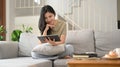 Smiling young asian woman in casual clothes using digital tablet on couch in cozy living room Royalty Free Stock Photo