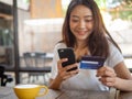 The smiling young Asian woman enjoys shopping online via a smartphone and paying online via credit card. Convenience of spending w Royalty Free Stock Photo