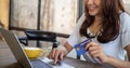 The smiling young Asian woman enjoys shopping online via a smartphone and paying online via credit card. Convenience of spending w Royalty Free Stock Photo