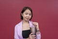 A smiling young asian woman in her mid 20s looking at the camera while taking a sip on a metallic tumbler. Wearing a pink blazer