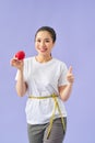 Smiling young asian woman holding measuring tape around her waist and eating red apple over violet background Royalty Free Stock Photo