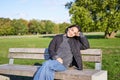 Smiling young asian woman in outdoor jacket, sitting on bench in green sunny park, resting alone, relaxing on fresh air Royalty Free Stock Photo