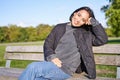 Smiling young asian woman in outdoor jacket, sitting on bench in green sunny park, resting alone, relaxing on fresh air Royalty Free Stock Photo