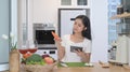 Smiling young asian woman reading online recipe on digital tablet and preparing vegetarian meal in the kitchen. Royalty Free Stock Photo