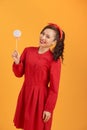 Smiling young Asian woman in red dress holding lollipop while standing over orange backgound Royalty Free Stock Photo
