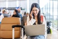 Smiling young asian woman sitting in waiting room and talking over smartphone with friend or family and using laptop. Beautiful Royalty Free Stock Photo