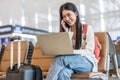 Smiling young asian woman sitting in waiting room and talking over smartphone with friend or family and using laptop. Beautiful Royalty Free Stock Photo