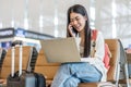 Smiling young asian woman sitting in waiting room and talking over smartphone with friend or family and using laptop. Beautiful Royalty Free Stock Photo