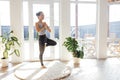 A smiling young Asian woman stands in the pose of a tree in the living room of the house. An attractive woman does yoga. House Royalty Free Stock Photo