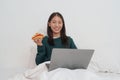 Smiling young asian woman using laptop computer in bedroom at home. lifestyle, woman lying on bed Royalty Free Stock Photo