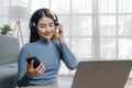 Smiling young asian woman using laptop web camera while wearing headphones and sitting on the rug beside to the sofa at Royalty Free Stock Photo