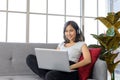 Smiling young asian woman wear casual clothing sitting on cozy couch, working on laptop computer while listen music at home Royalty Free Stock Photo