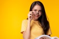 Smiling young asian woman wear eyeglasses holding book and looking at camera with smile face and happiness over yellow background, Royalty Free Stock Photo