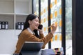 Smiling young asian woman writing on sticky notes on window in creative office Royalty Free Stock Photo