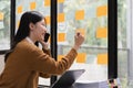 Smiling young asian woman writing on sticky notes on window in creative office Royalty Free Stock Photo