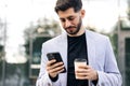 Smiling young attractive bearded man walking use smartphone look around at city center. Handsome man messagen stylish Royalty Free Stock Photo