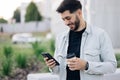 Smiling young attractive bearded man walking use smartphone look around at city center. Handsome man messagen stylish Royalty Free Stock Photo